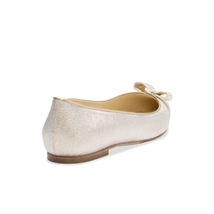 Rear three-quarter view of Natalie flat showcasing champagne lamé textured upper, decorative bow, and low stacked heel on plain background